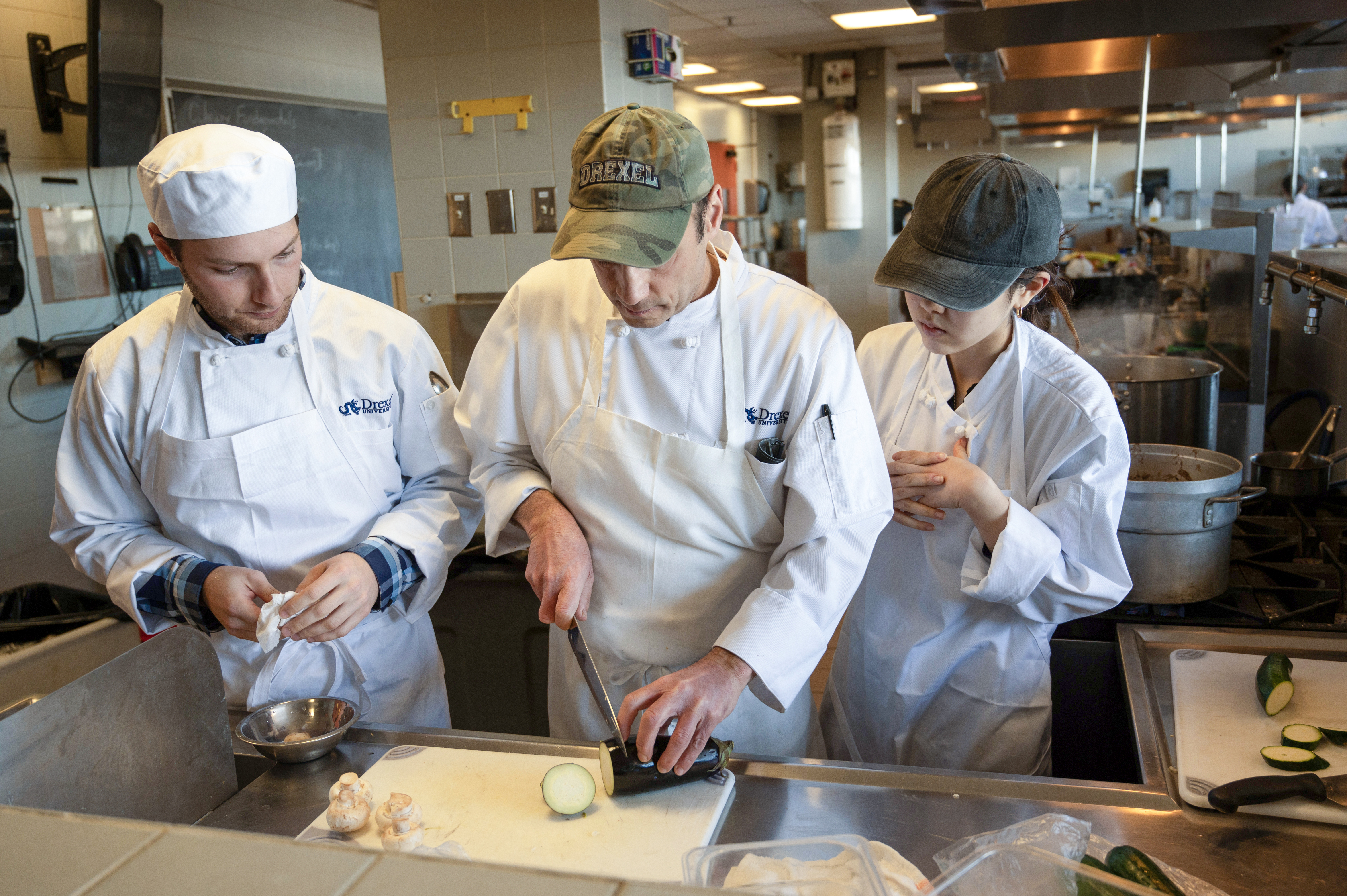 faculty member demonstrates to two students how to slice cucumber